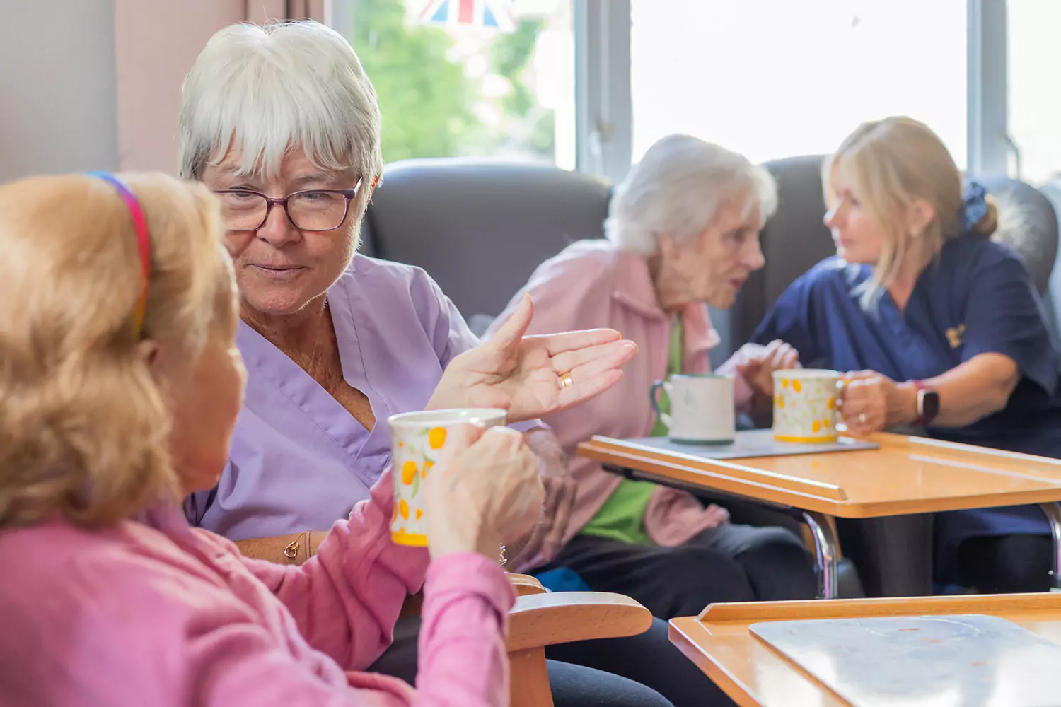 Residents and care staff chat over a cup of tea in the lounge